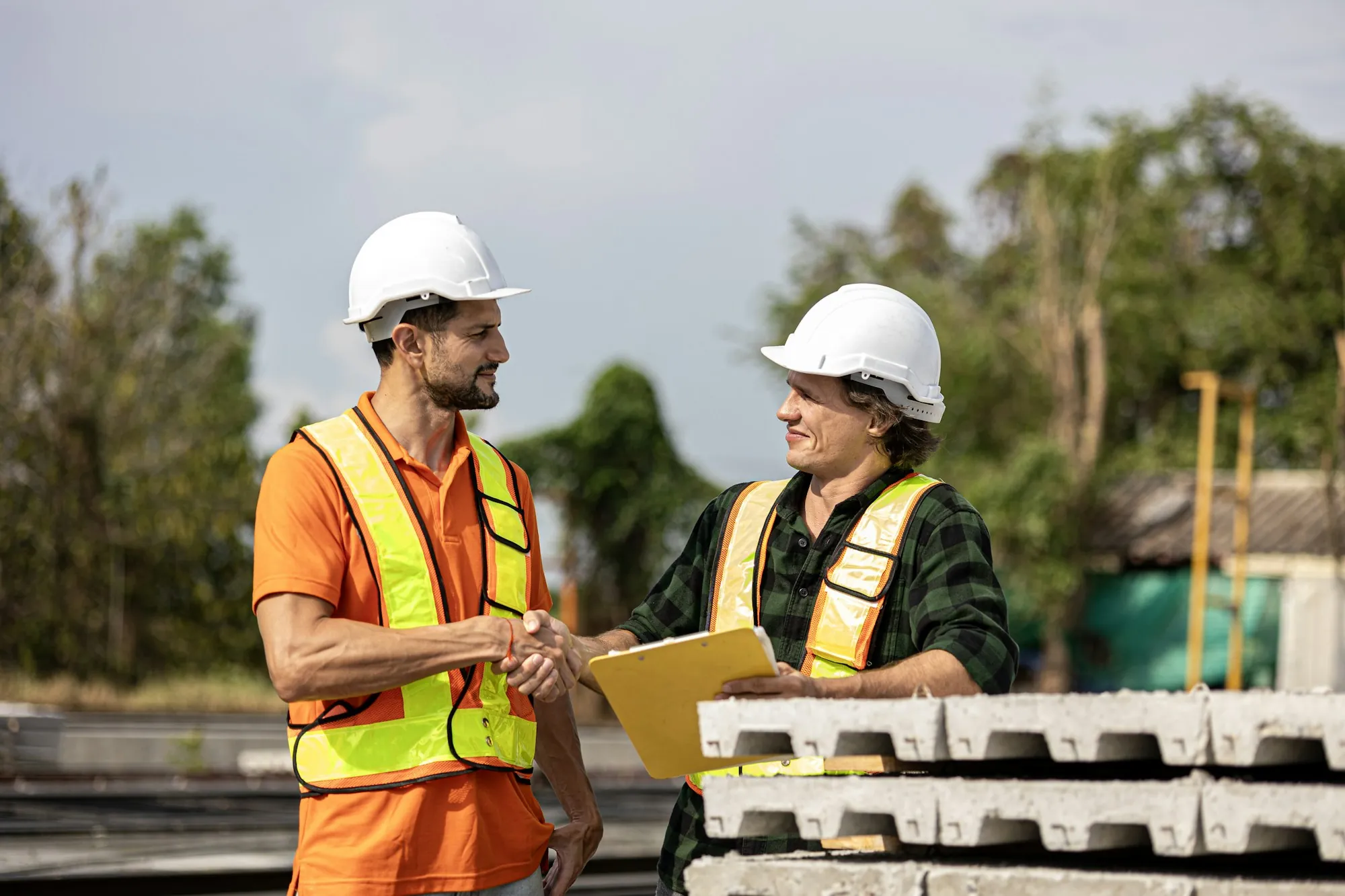 Two workers in hard hats talking over paperwork outdoors